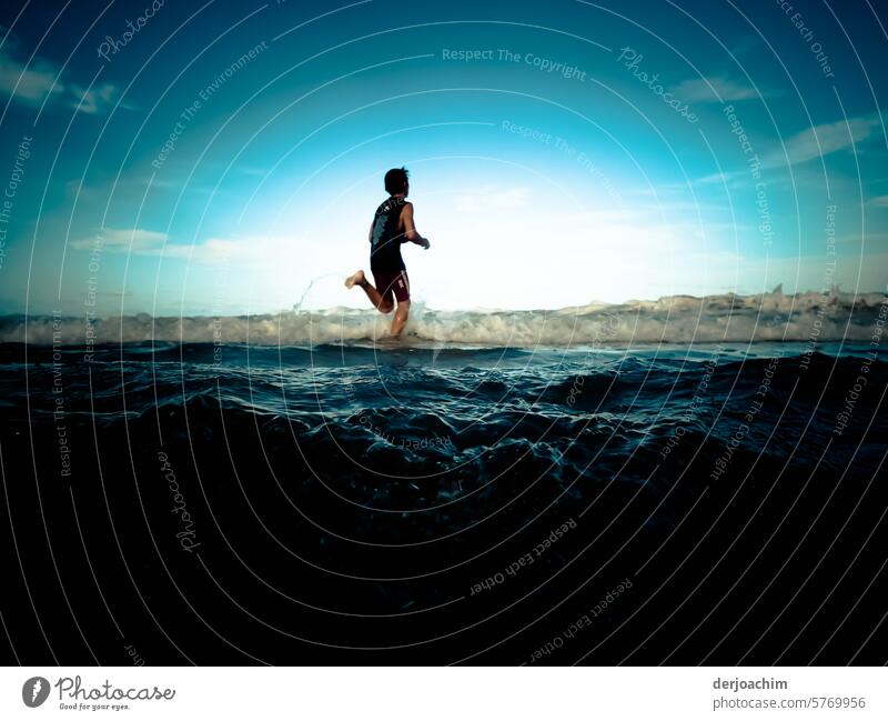 A child runs along the beach through the dark blue shimmering water. The background is bright and there are almost no clouds to be seen. Beach Blue coast Water