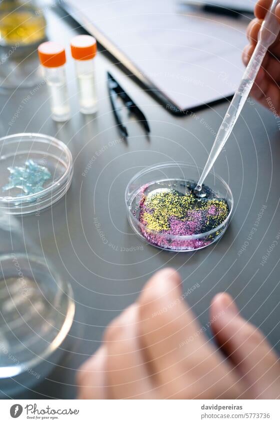 Female chemist adding drop of liquid from from pipette over petri dish with mix of glitters in lab female chemistry hands dropper sample micro plastic