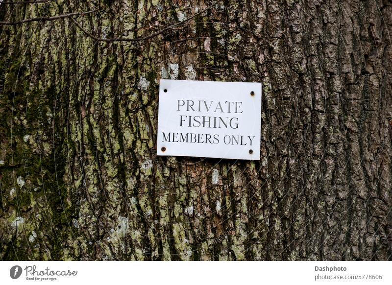 Private Fishing Sign Attached to a Tree Trunk in a Rural Location sign signpost signboard signage text wording nails nailed attached rust rusty rusting