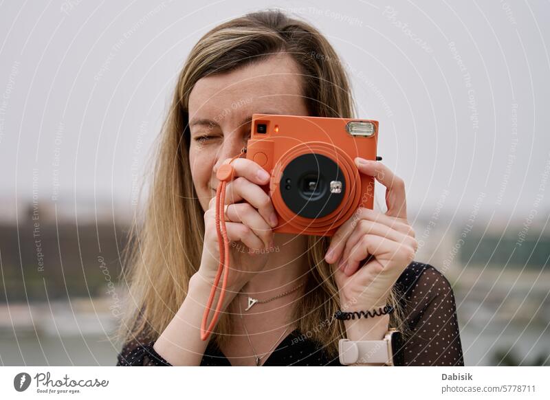 Female traveler taking picture with vintage instant camera tourist photo woman tourism photography memories scenic daytime capture orange retro nostalgia