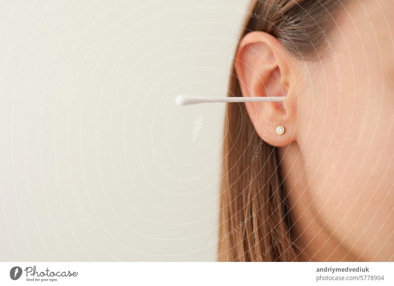 Cropped shot of unrecognisable young woman with cotton swab in ear isolated on white background. Close up female uses hygienic stick for cleaning ear. Daily habit routine. Hygiene and health care.