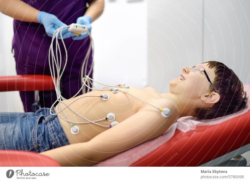 Child under ECG test with doctor. Boy patient lying in medical bed with vacuum sensors. A nurse performs an electrocardiogram of the heart in office of a medical clinic. Checkup of heart