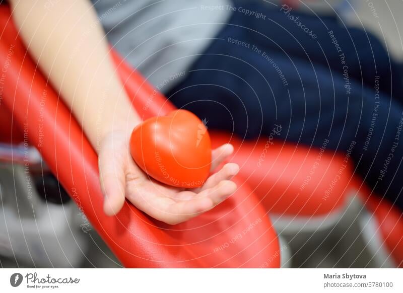 A nurse takes blood from a child. Close up view of kid hand with a bouncy heart shape ball during of taking a blood sample for examination in a modern laboratory or hospital. Baby health check