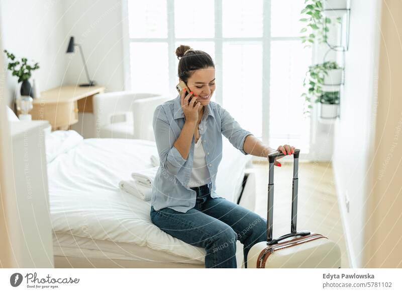 Young woman with a suitcase sitting on bed in hotel room and using phone packing clothing vacations travel preparation people luggage one person bag tourism