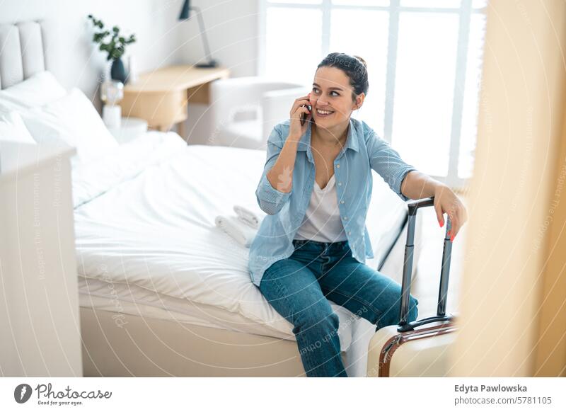 Young woman with a suitcase sitting on bed in hotel room and using phone packing clothing vacations travel preparation people luggage one person bag tourism