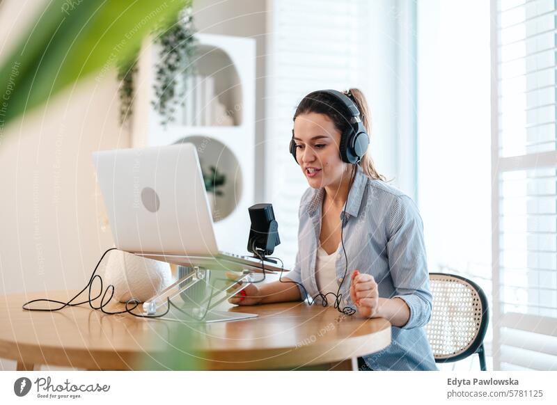 Woman wearing headphones sitting at a desk speaking into microphone and recording a podcast woman people one person room living room adult young young adult