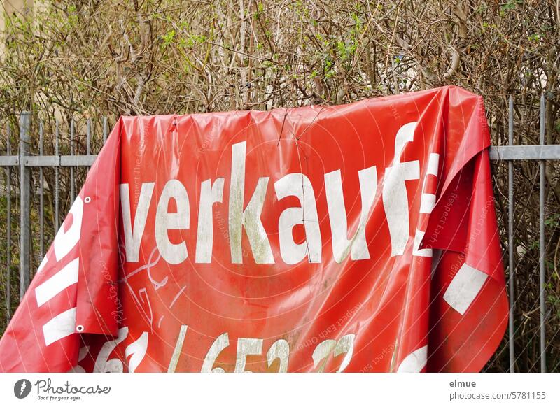 Red PVC advertising banner hanging in folds on a metal fence with the inscription - for sale - Offer quote Metalware Real estate sales Distribution remunerated