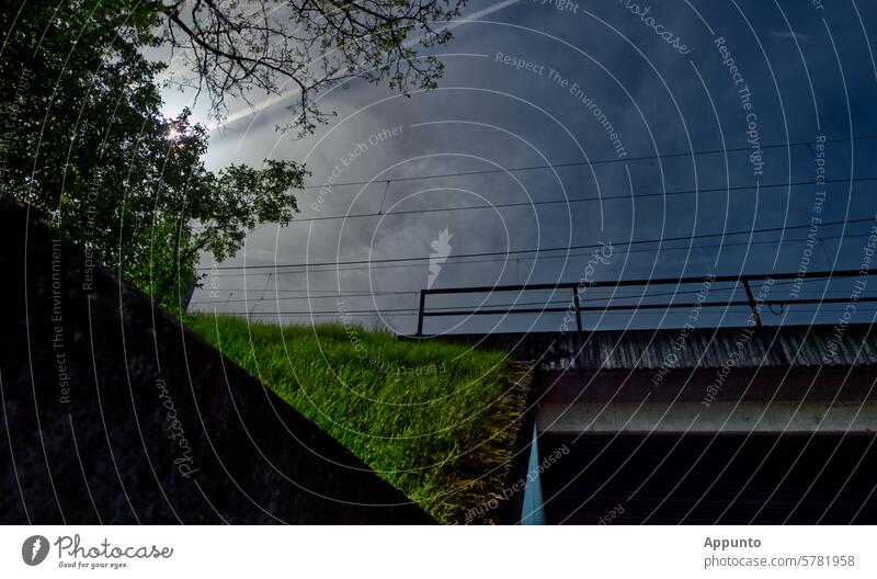 Geometry in everyday life: urban scene of concrete, grass, light and sky on a green railroad embankment with the entrance to a concrete railroad underpass lines