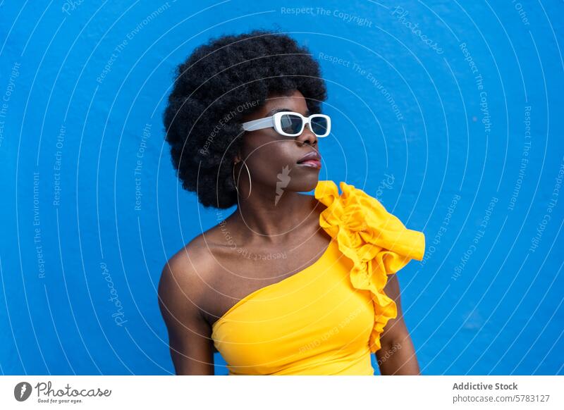 Fashionable Afro Woman with Striking Blue Background afro woman fashion style sunglasses yellow dress blue background vibrant confident pose elegant chic trendy