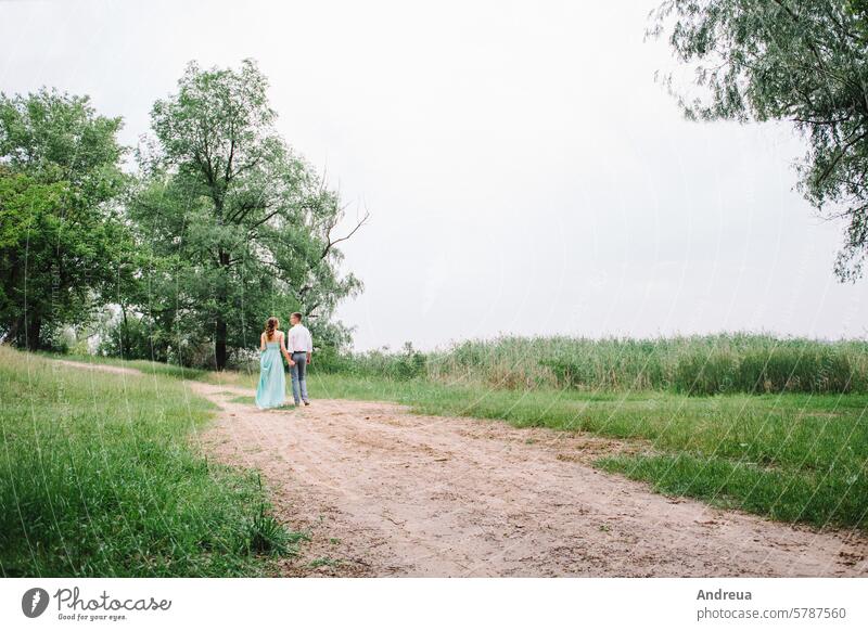 happy guy in a white shirt and a girl in a turquoise dress are walking in the forest park young grass trees bushes green brown day summer spring love nature