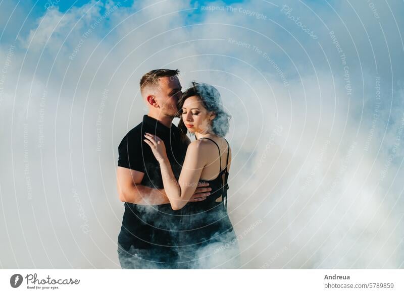 guy and a girl in black clothes hug inside a  smoke beach sand day blue clothing youth together thick escape fire forever water sky background