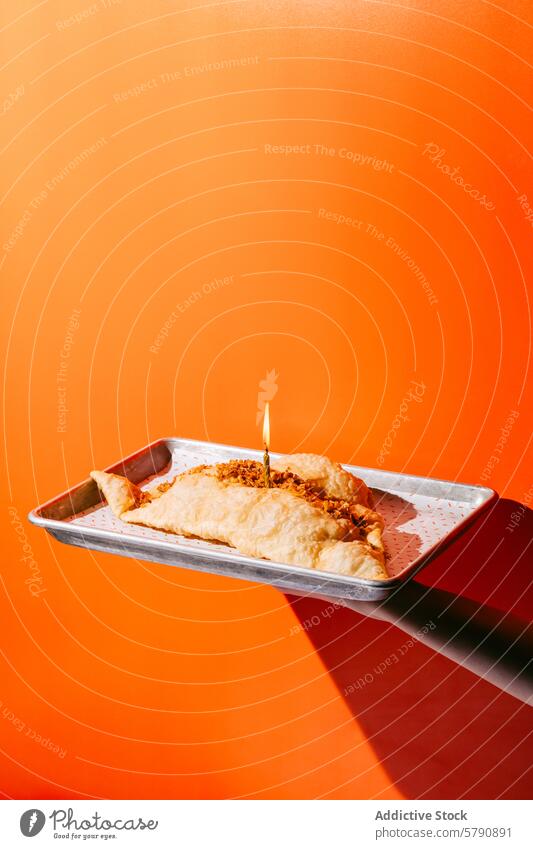 Savory Baked Cheburek on a Tray with Festive Candle baked cheburek tray metal lit candle celebration savory orange background festive cuisine pastry