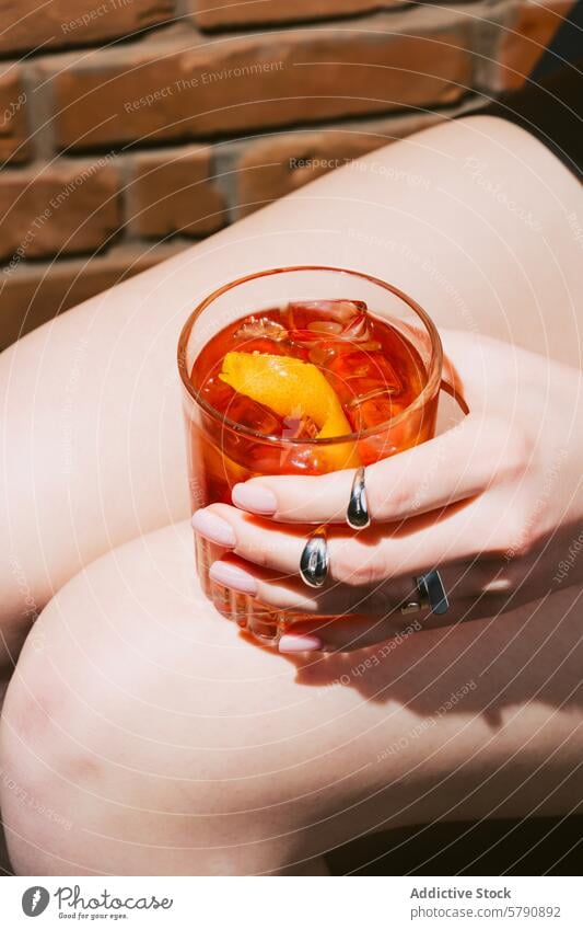 Close-up of a refreshing Negroni cocktail held in hand negroni glass ice orange peel refreshment leisure drink beverage alcohol close-up sunlight summer fingers