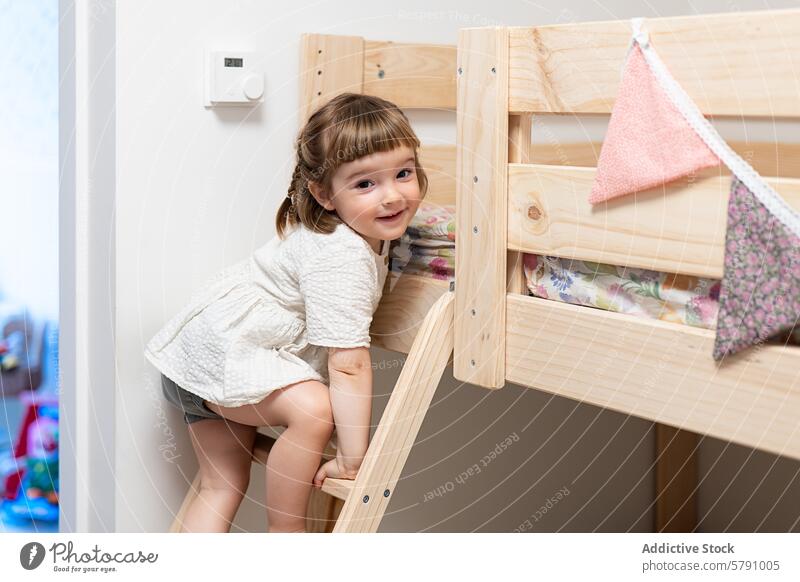 Child climbing a wooden bunk bed with a playful smile child girl ladder room clean bright cheerful happy indoors home bedroom furniture bedtime sleepover fun