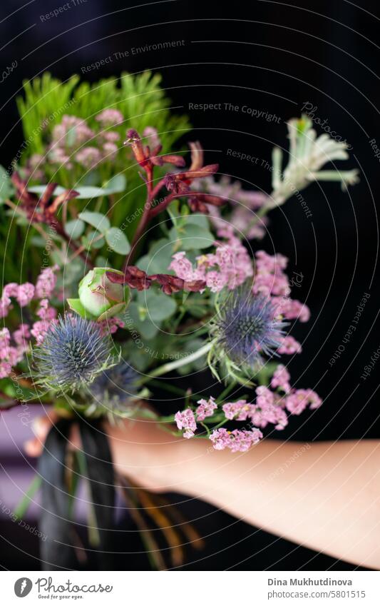 flower bouquet arrangement with exotic Eryngium flower bloom and green conifer plant on  vertical black background with copy space blossom decoration flora