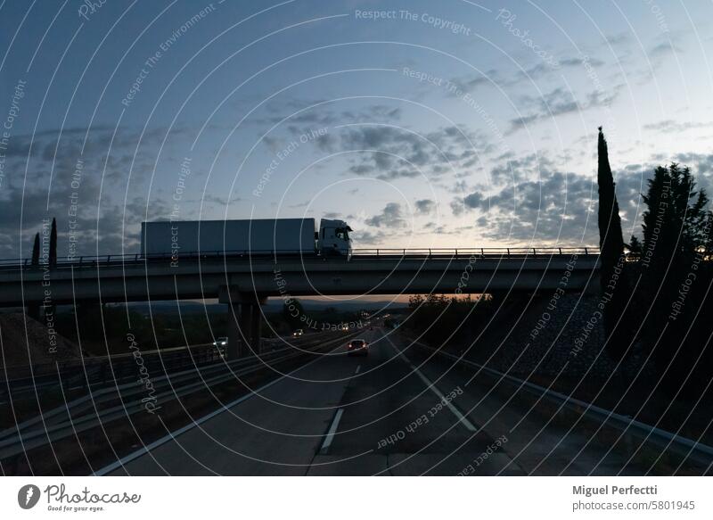 Highway at dusk with vehicles and a bridge with a truck driving, side view of the truck. highway transport logistic sunset freight lorry road traffic motorway