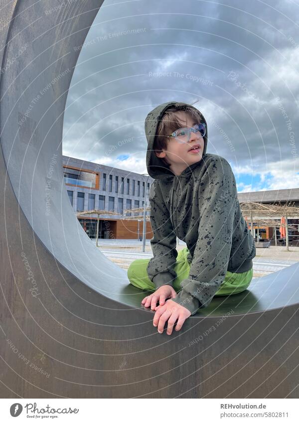 Boy sitting in a sculpture Child Infancy Boy (child) portrait Face naturally Authentic fun Exterior shot Future Looking Brash teenager Hooded (clothing) campus