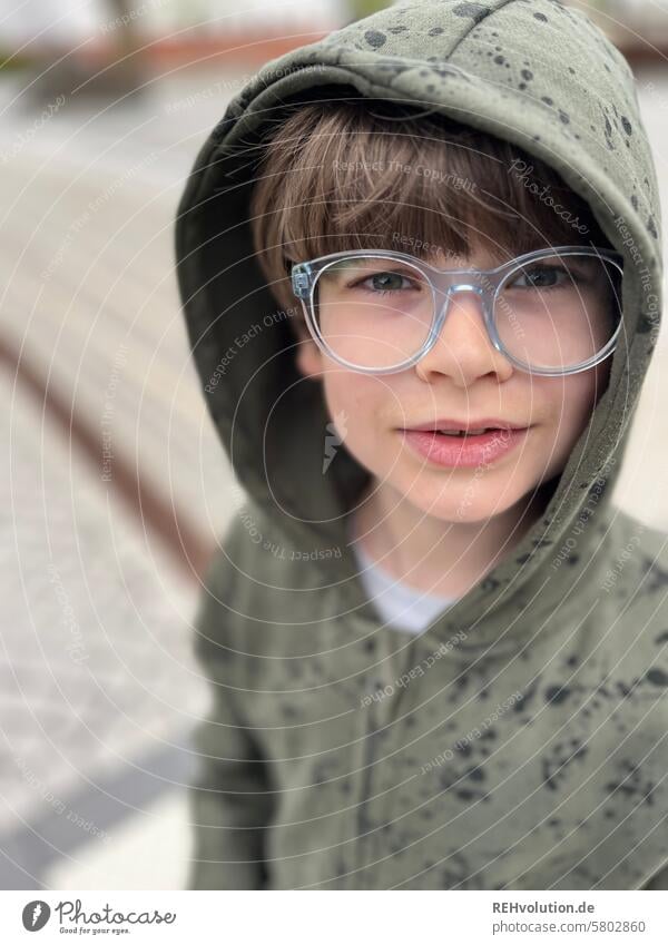 Boy with glasses looks irritated Child Infancy Boy (child) portrait Close-up Exterior shot Authentic Front view blurriness Upper body Hooded (clothing) teenager