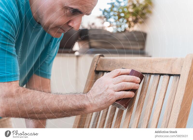 Craftsman Sanding a Wooden Chair for Restoration craftsman sanding wooden chair restoration varnishing outdoor meticulous woodwork furniture renovation hand