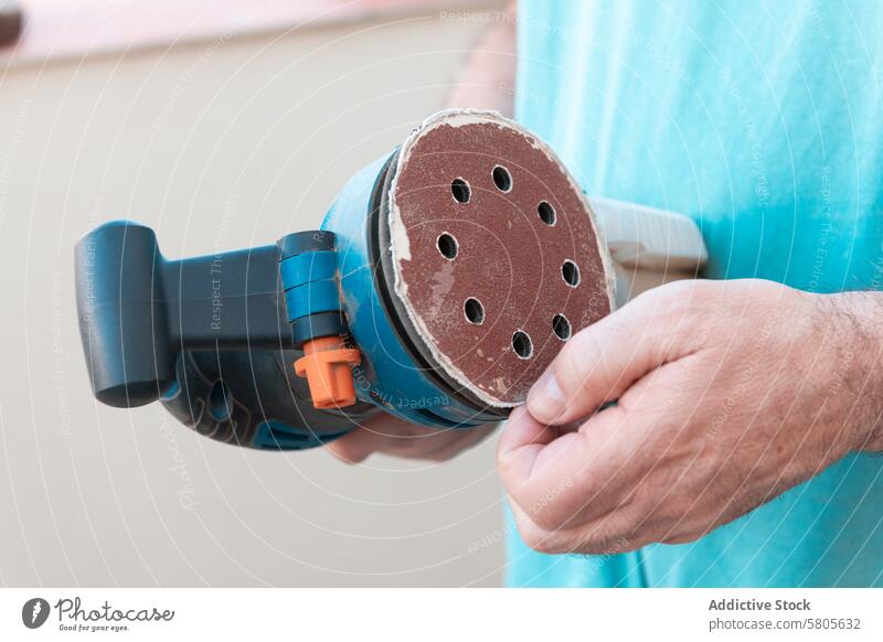 Close-up of man using an orbital sander on wood sanding furniture restoration varnishing carpentry woodworking tool electric equipment close-up hand manual