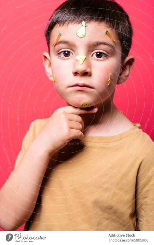 Boy with fruit stickers on face over pink background boy child adhesive portrait contemplative looking at camera expressive school kid playful innocence youth