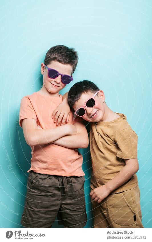 Two happy school boys posing with sunglasses child kid smile cheerful confidence pose blue background looking at camera t-shirt summer friendship young style