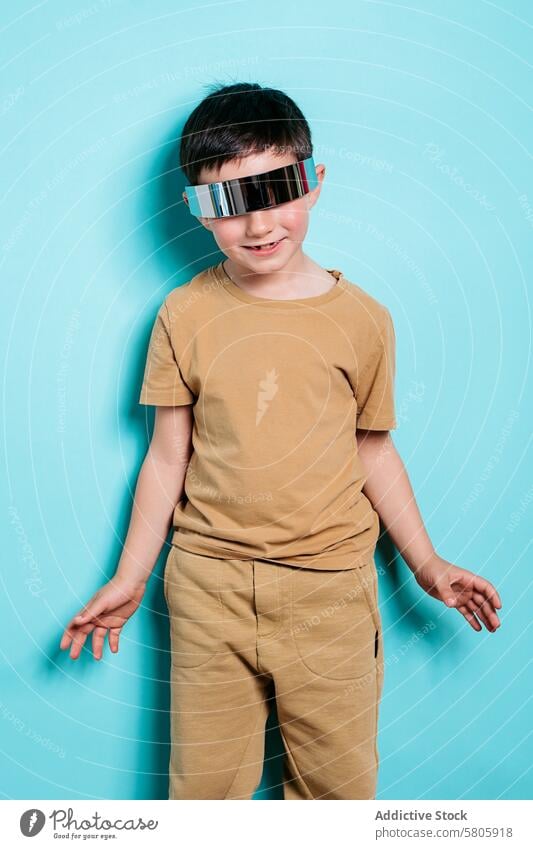 Boy with futuristic sunglasses posing on turquoise background boy casual outfit tan reflective smile joy vibrant fashion style modern kid school youth trendy