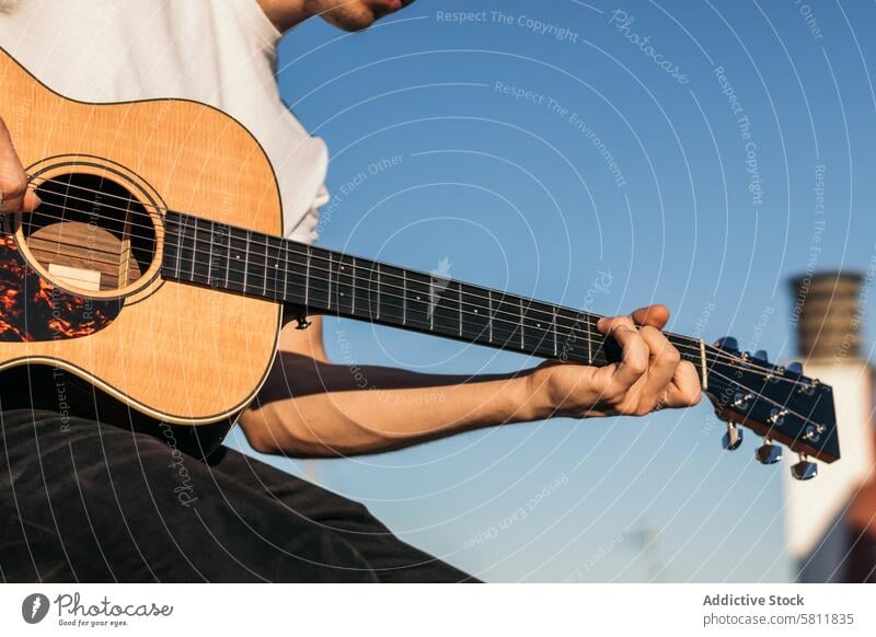 young man sitting playing acoustic guitar on a rooftop. close-up musician guitarist male person instrument player musical casual rock people caucasian handsome