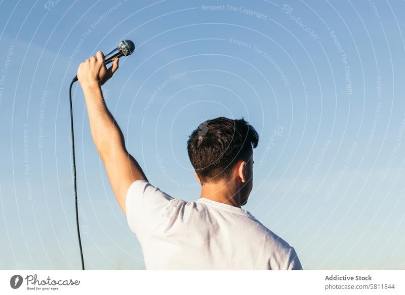 back view of a man with arm raised holding a microphone singer young music entertainment people person performer performance musician song background singing