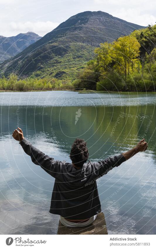 Carefree traveling man enjoying freedom near lake in mountains traveler carefree outstretch highland pond pyrenees male nature ridge rock admire pier adventure