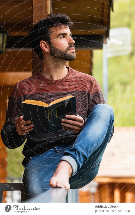 Pensive man chilling on terrace with book read ponder thoughtful vacation house veranda literature male pyrenees rest relax wooden enjoy sit peaceful tranquil