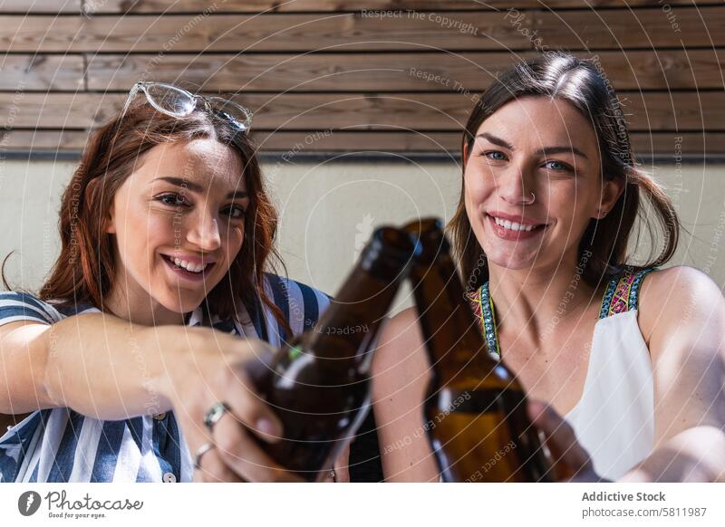 Cheerful girlfriends with beer spending weekend on sofa cheers interact cheerful spend time lifestyle portrait women smile chill alcohol drink bottle beverage