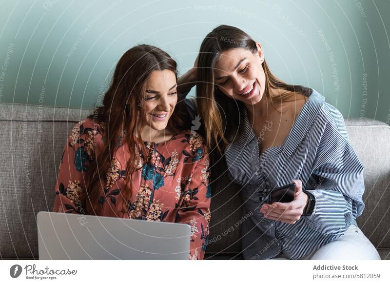 Young women resting on sofa and browsing smartphones using together calm comfort friend gadget living room chill cozy young modern mobile girlfriend surfing