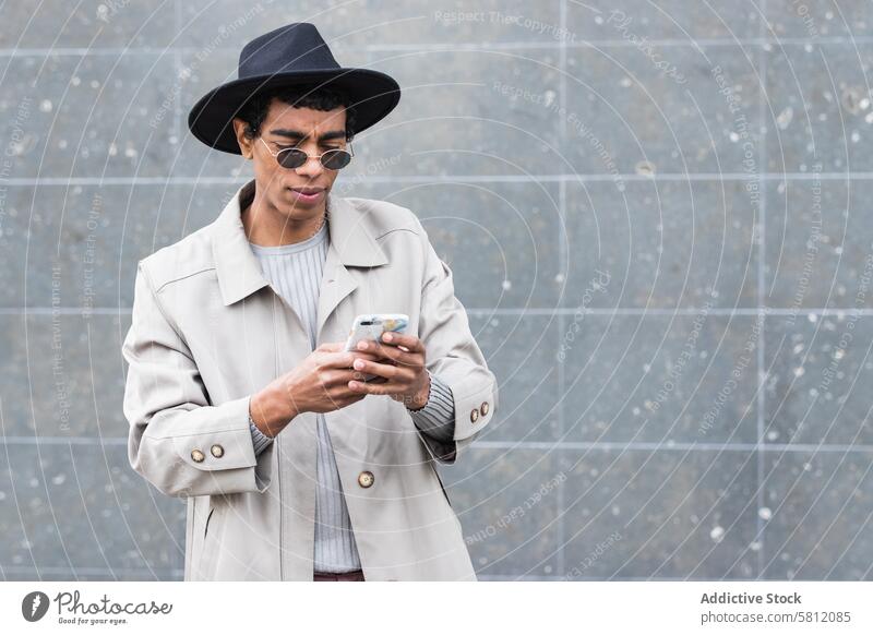 Stylish ethnic man with smartphone on street enjoy trendy wireless using gadget device internet online cellphone hat garment fashion style masculine male