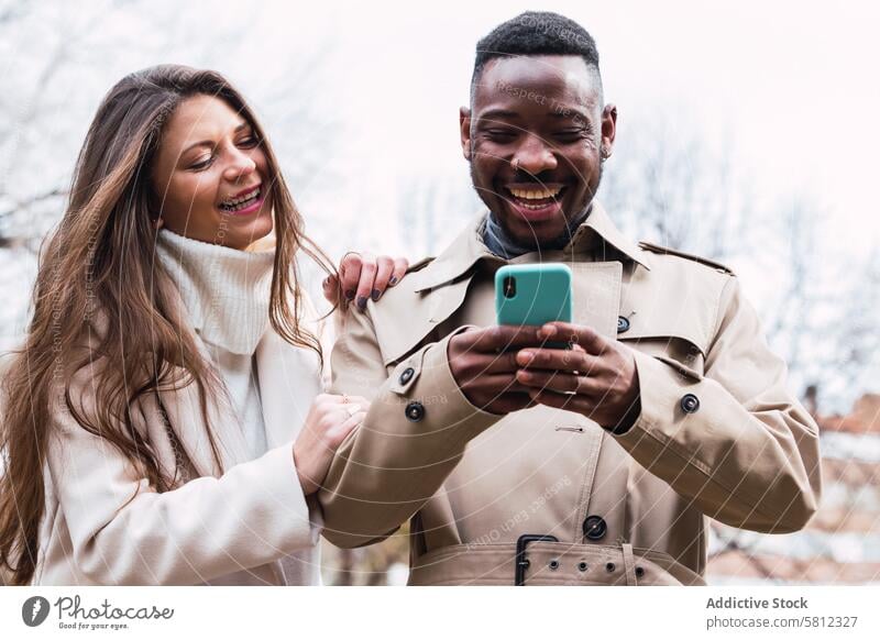 Joyful multiethnic couple using smartphone in park happy together mobile romantic love content adult multiracial diverse african american black news