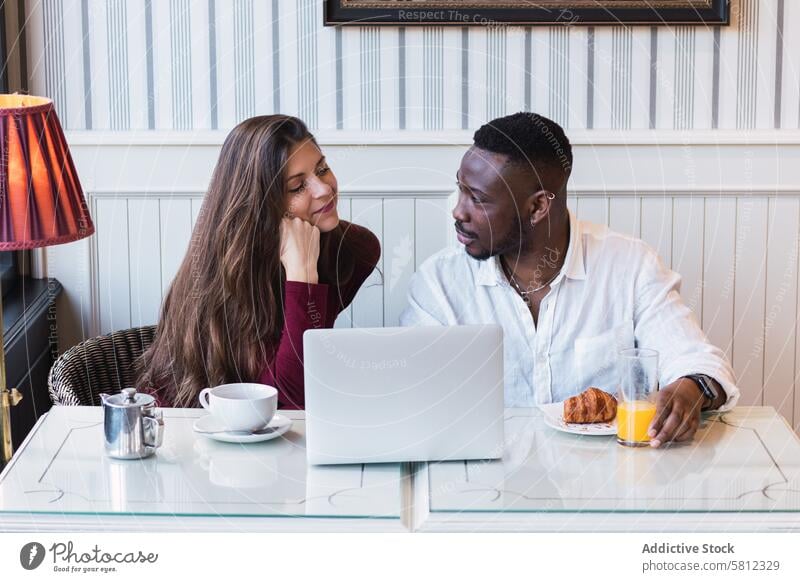 Cheerful multiethnic couple using laptop during breakfast at home together happy relationship cheerful browsing watch multiracial diverse black african american