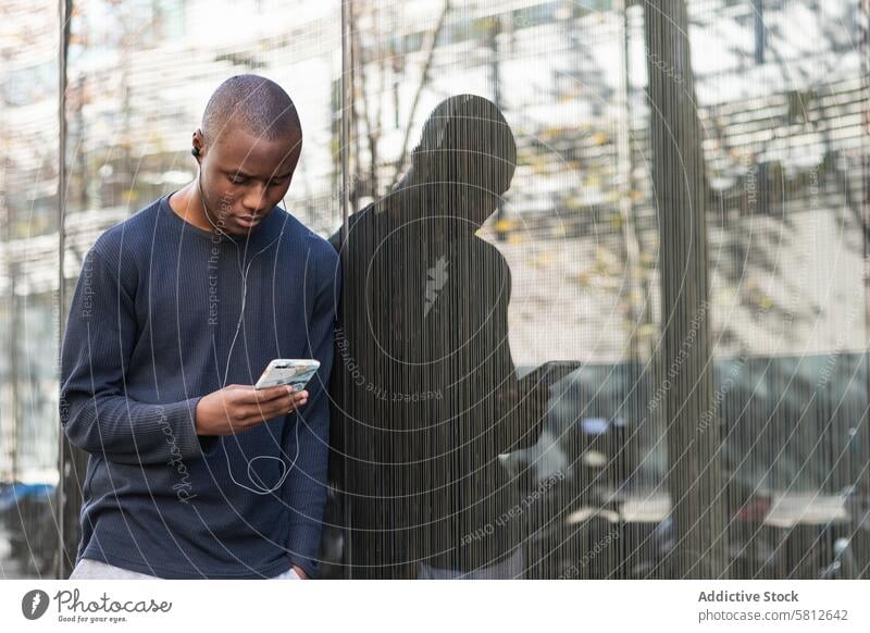 Serious black man using smartphone against gray wall serious headphones text message attentive music watch check read digital male mobile surfing browsing