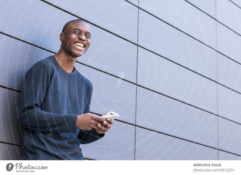 Happy black man using smartphone against gray wall text message happy smile watch check read digital male mobile surfing browsing cellphone connection guy