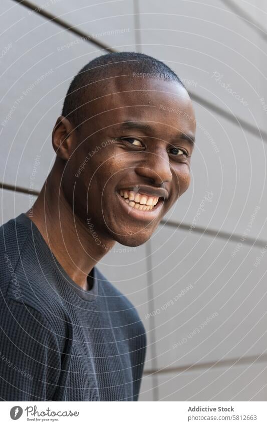 Happy young African American male standing near wall man casual happy style masculine ponder town alone black knitted garment denim ornament rough wistful