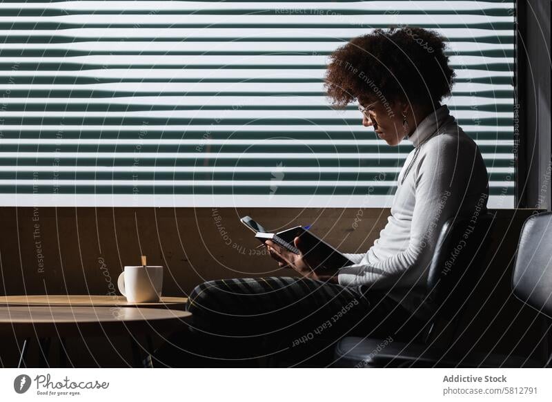 Focused young black guy taking notes while chilling in cafe with cup of coffee man take note student concentrate homework assignment education smart study focus