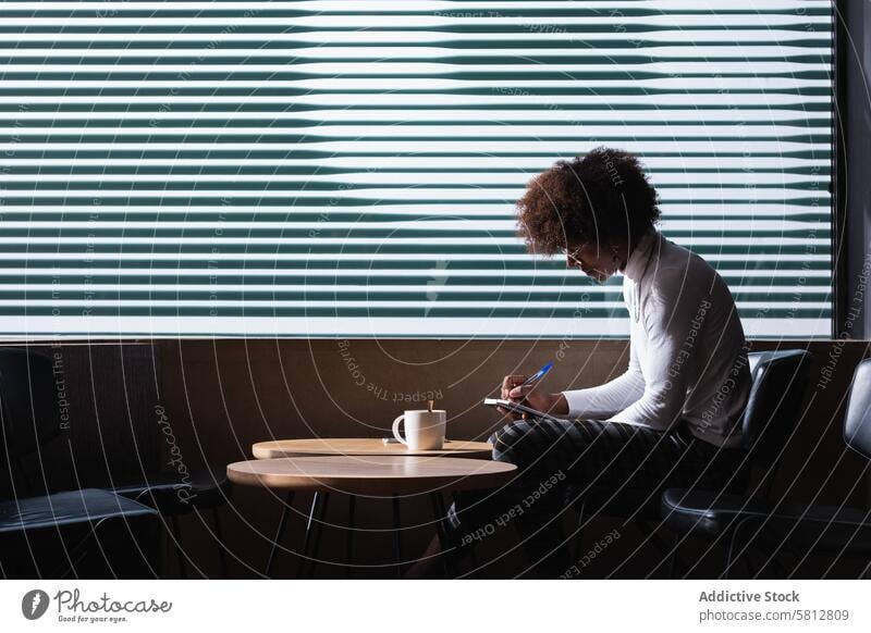 Focused young black guy taking notes while chilling in cafe with cup of coffee man take note student concentrate homework assignment education smart study focus