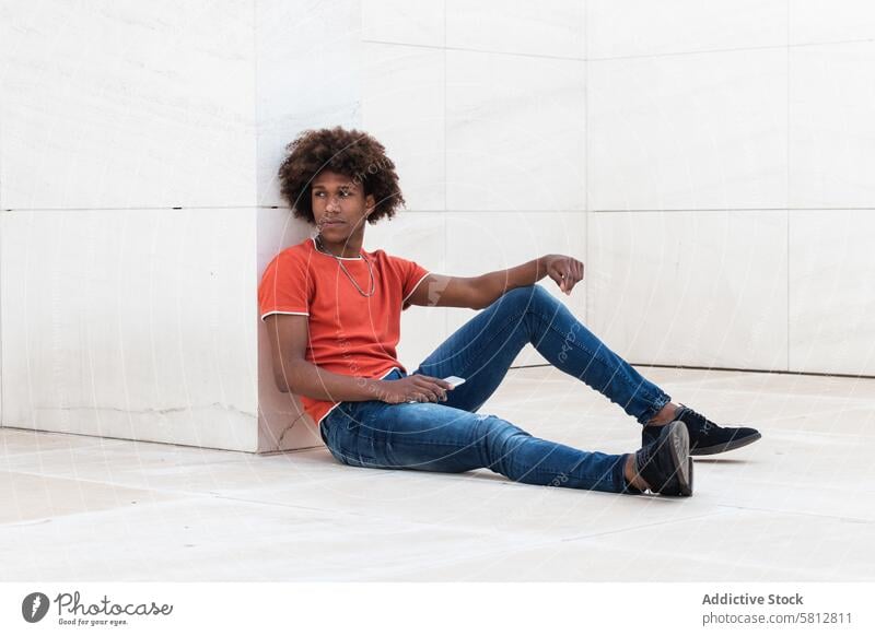 Concentrated young ethnic man sitting on floor and holding smartphone serious sms digital message chat focus online mobile african american man black man casual