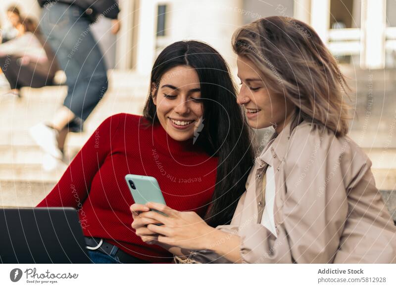 Two student girls sitting on the stairs of the college with the laptop and the mobile. Close-up young education people female computer two studying students