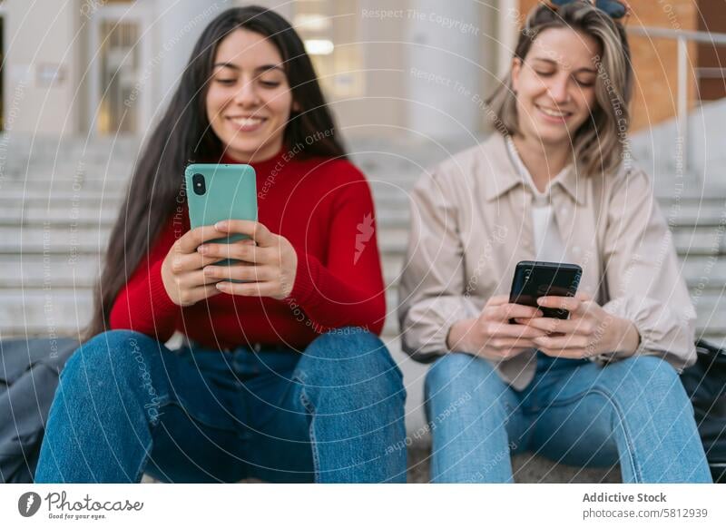 two student girls sitting on the stairs watching the mobile young friends phone female internet students people couple smartphone happy caucasian university