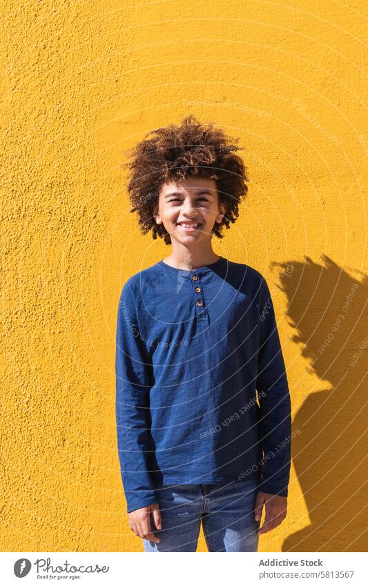 Ethnic boy with curly hair standing on yellow wall afro colorful bright kid teen gesture positive male child african american black ethnic teenage vibrant