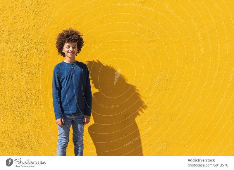 Ethnic boy with curly hair standing on yellow wall afro colorful bright kid teen gesture positive male child african american black ethnic teenage vibrant