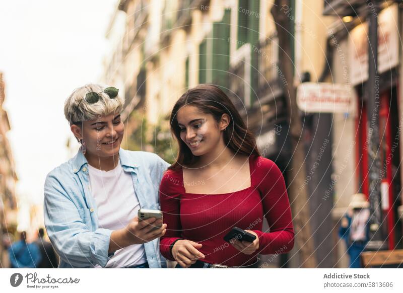 two teenager girls walking and watching something her mobiles outdoors communication cheerful internet young talking people family two people lifestyles