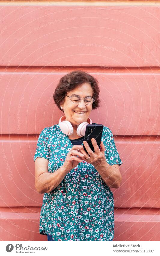 Old woman using smartphone and listening to music with headphones stylish mobile cellphone senior female communication device message lifestyle internet