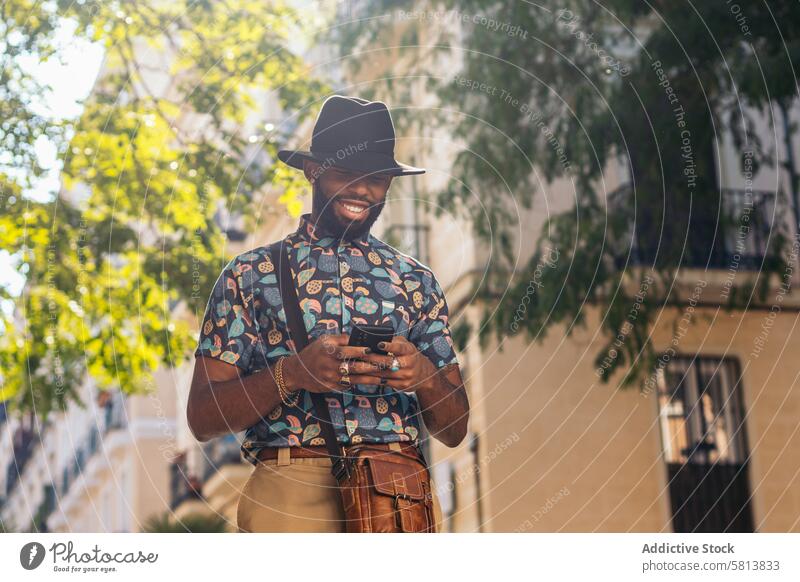 Stylish black man walking on the city street using smartphone technology lifestyle young urban mobile male person cellphone stylish guy outside people casual