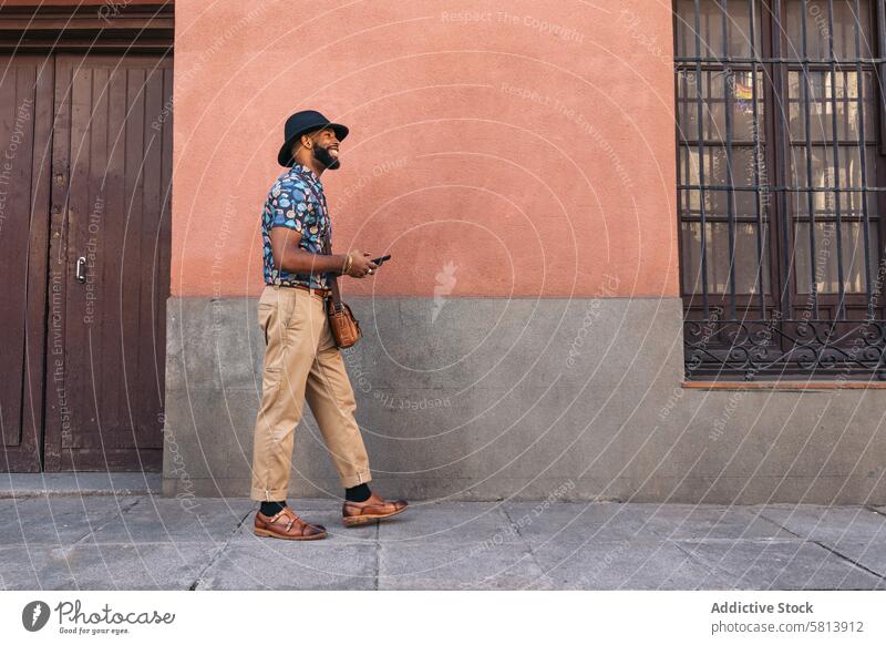 Stylish black man walking on the city street using smartphone technology lifestyle young urban mobile male person cellphone stylish guy outside people casual